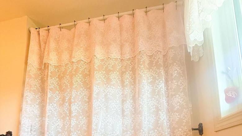 A white lace shower curtain with a valance hangs from a rod in a bathroom.