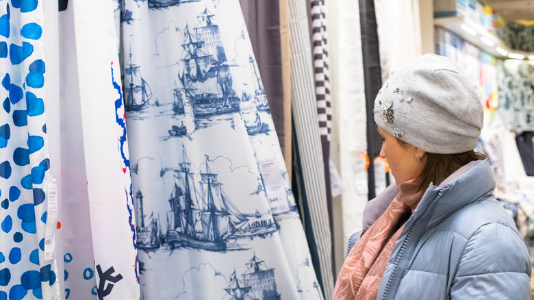 A woman looks through a selection of shower curtains on display in a home decor store.