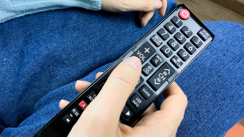 A person's hand holding a tv remote over their lap
