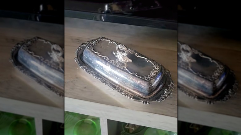 A mirrored image of silver butter dish on a shelf in a TV room