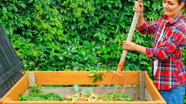Person using a pitchfork to mix material in compost bin