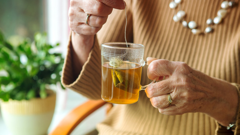 A person holding a glass cup with a steeping tea bag inside