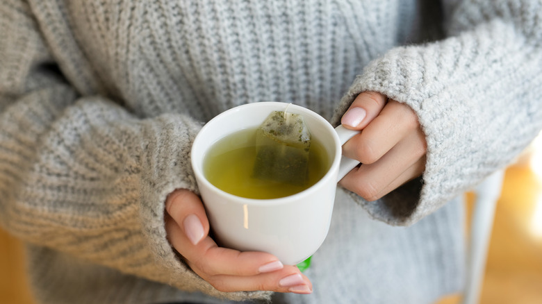 Person holding a cup of hot green tea.