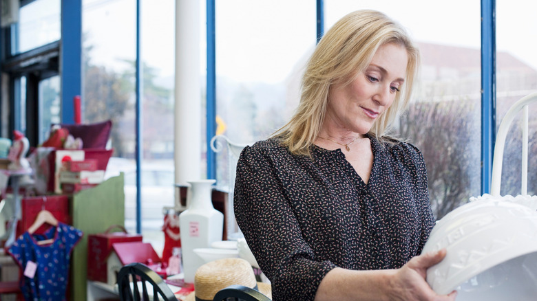 A woman looking at a white ceramic bowl in a thrift store.
