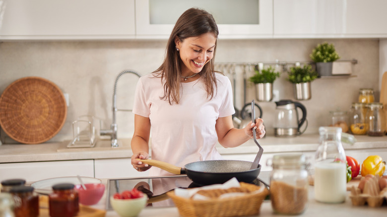 a woman prepping food and cooking with a frying pan in the kitchen