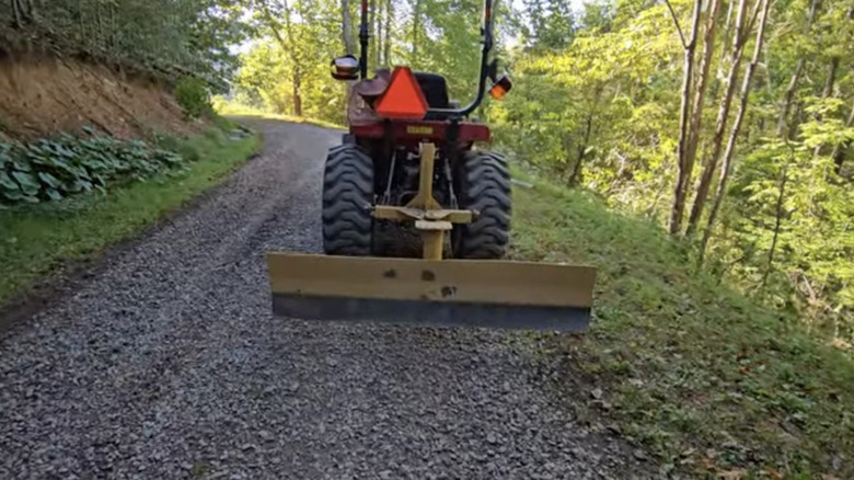 tractor with the attachment on a large driveway with shrubs on either side