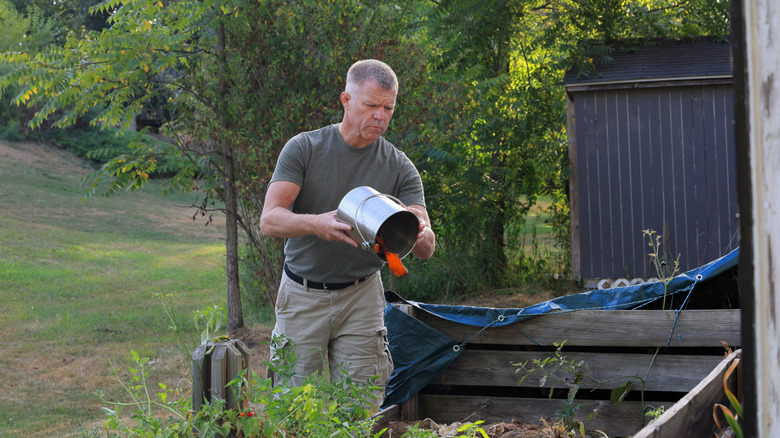 A man throws some items into a large compost pile in his backyard.