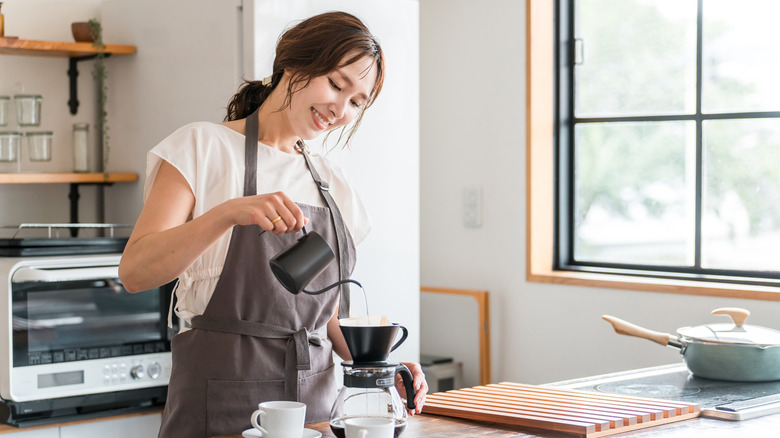 Woman in apron pouring hot water into a coffee maker