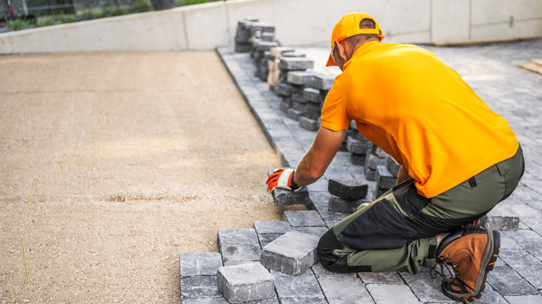A man in a yellow shirt and hat placing pavers down on smoothed sand