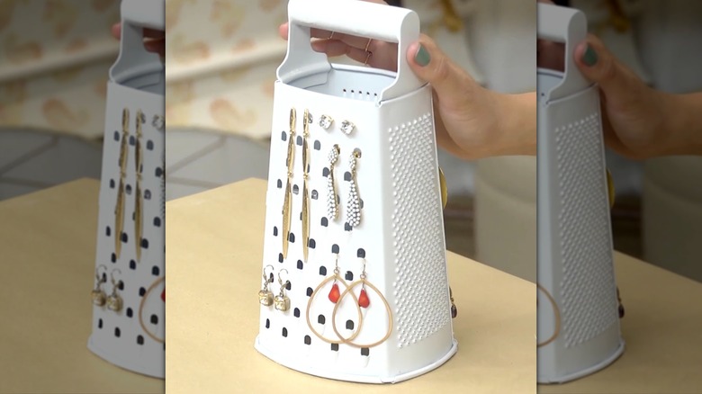 Cheese grater painted white and turned into an earring holder sitting on a table.