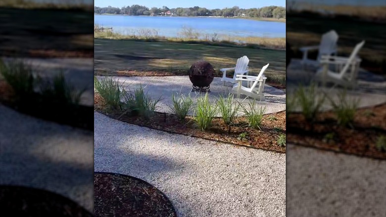 Backyard fire pit and garden path made of crushed seashells lined with mulched garden beds in front of a body of water