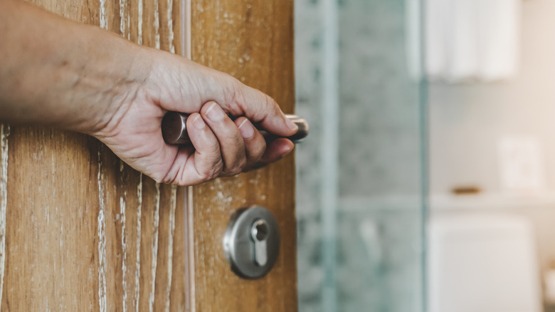 Person's hand using door knob to open wooden bathroom door.
