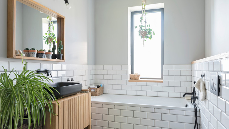 A bathroom with white subway tiles, a bathtub, and plants.