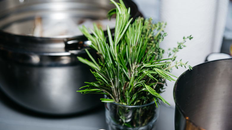 A glass of cut fresh herbs sitting next to a silver pot