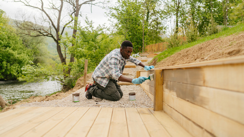 Man staining a wooden retaining wall