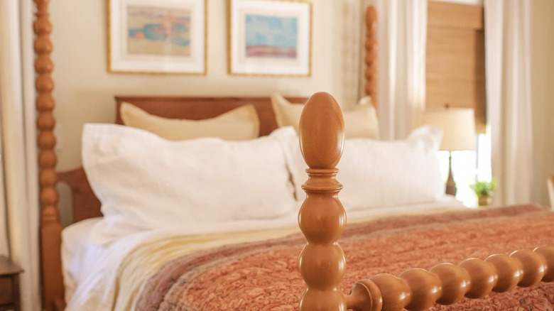 Erin Napier's bedroom, featuring a four-poster wooden bed, a variety of pillows and fabrics, and framed artworks on the wall.