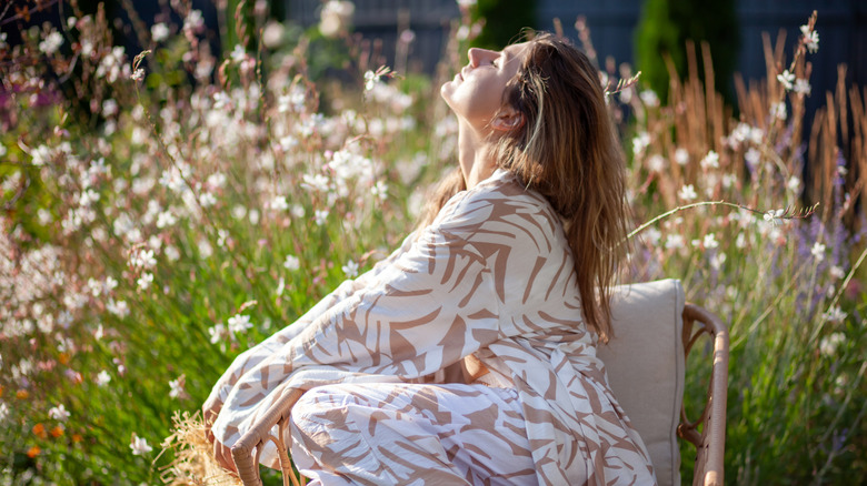A woman is relaxing in her garden, with white gaura flowers in blurry background