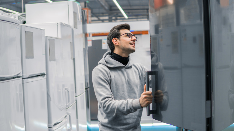 Man wearing a gray hoodie and glasses browses refrigerator models at a store.