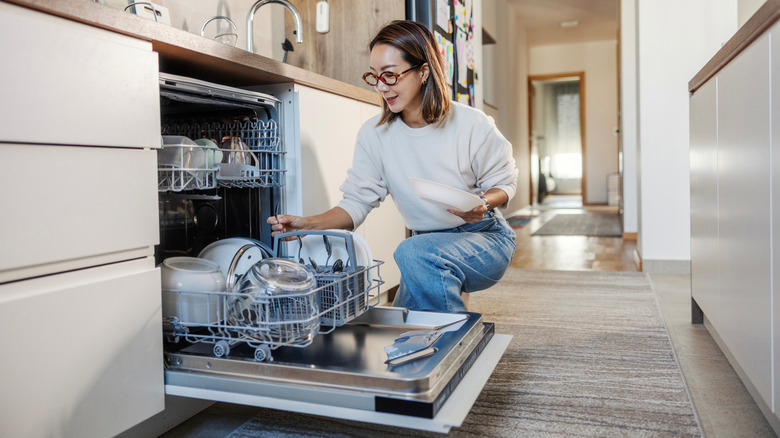 A woman adding dishes to her dishwasher by kneeling down