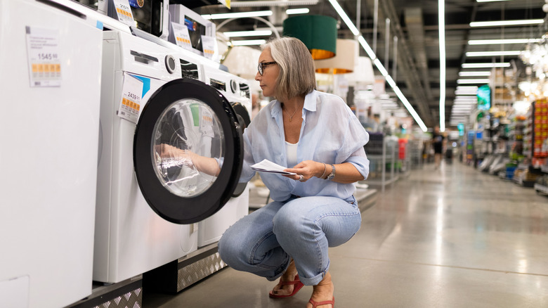 A woman crouches down to inspect a clothes washer in a large home improvement store.