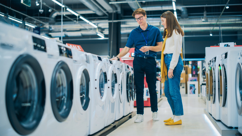 A sales representative assists a young woman as she shops for washers in a large department store.
