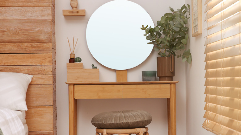 A vanity with a mirror and a stool next to a bed.