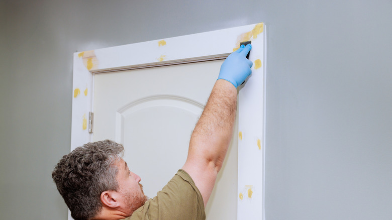 a man works on the door frame trim using wood putty to fill cracks and holes