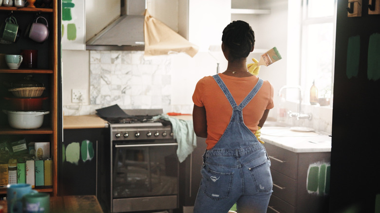A woman wearing overalls questioning her paint color decisions in a kitchen