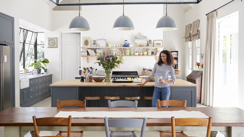 A woman standing by a kitchen island and holding a cup of coffee