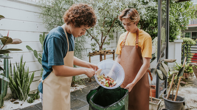 Two people standing outside and dumping food scraps into a bin for composting