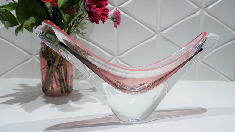 A sommerso glass bowl with layered pink and clear glass in front of a vase