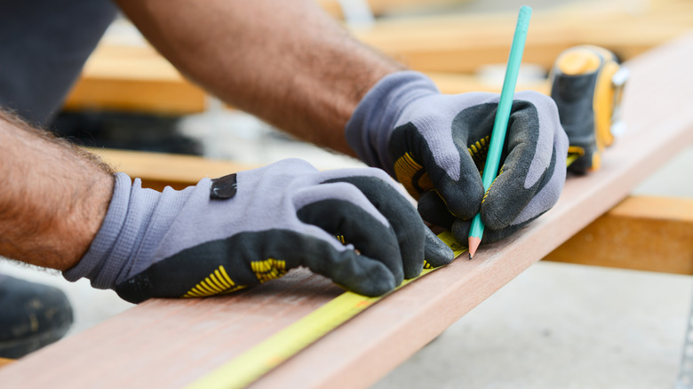 Close-up of a person with gloves and a pencil marking wood planks during floor installation