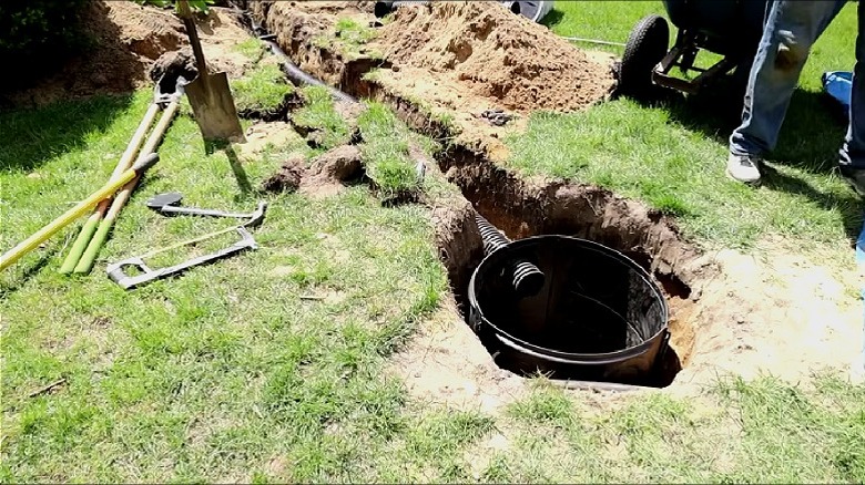 A dry well installed in the ground of a grassy yard with a single drainage inflow pipe.