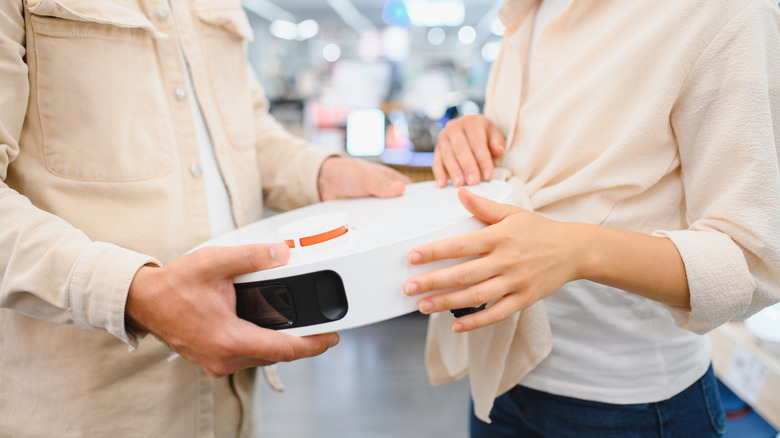 Customers holding robotic vacuum cleaner, shopping in home appliance store