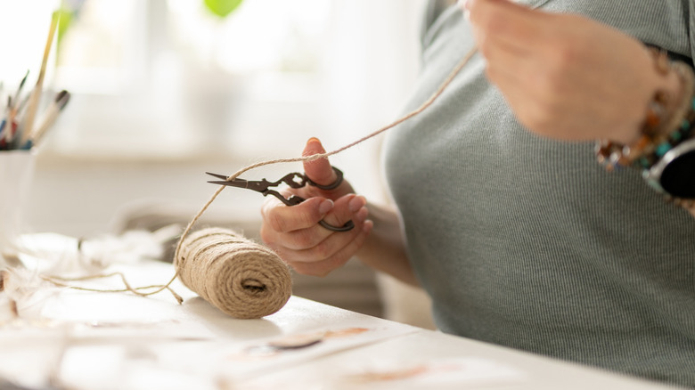 Person cutting through a roll of twine with small scissors at a craft bench
