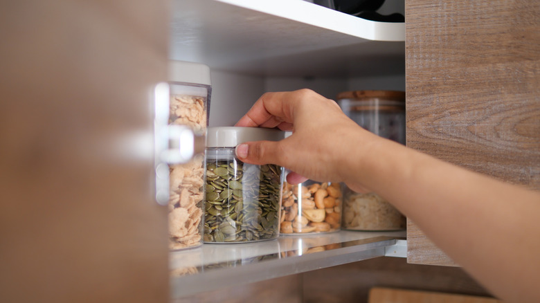 Hand reaching for a jar in a cabinet.