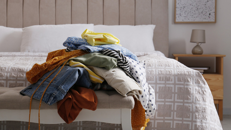 pile of clothes on bench at the end of the bed