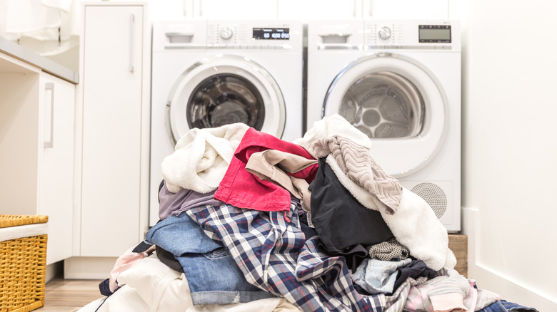 A messy pile of clothes sits on the floor in front of a washer and dryer.