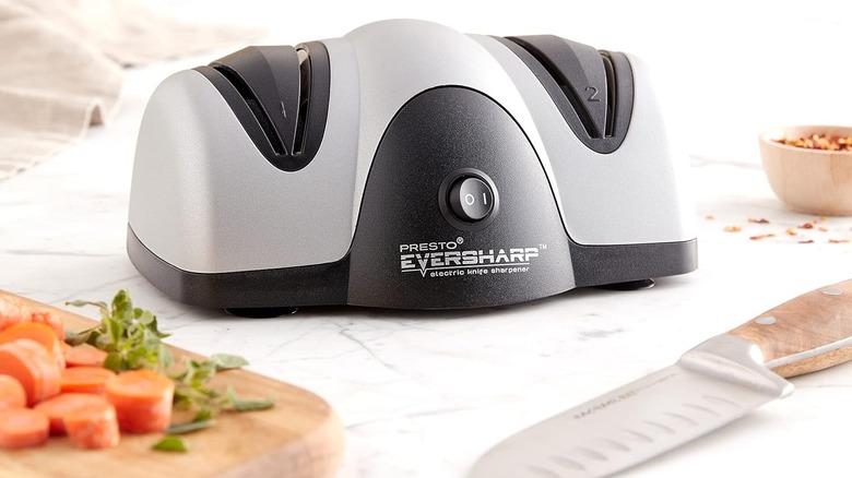 Electric knife sharpener on a countertop next to a knife and a cutting board with vegetables on it