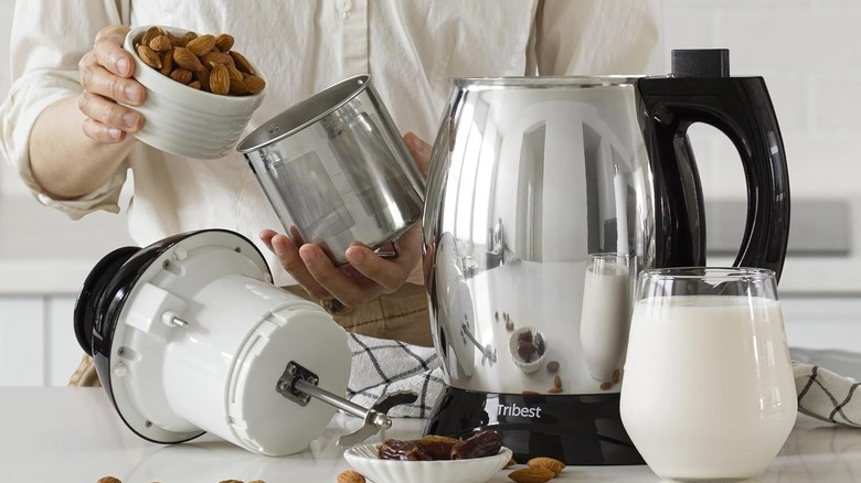 Person pouring almonds into the container of a nut milk making machine