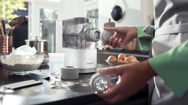 Home chef putting attachments on an automatic pasta maker with pasta ingredients on the countertop