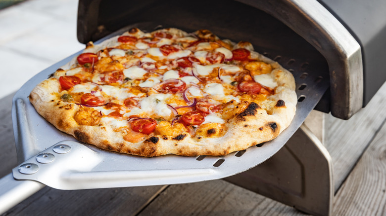 Pizza being put into a small pizza oven on a patio
