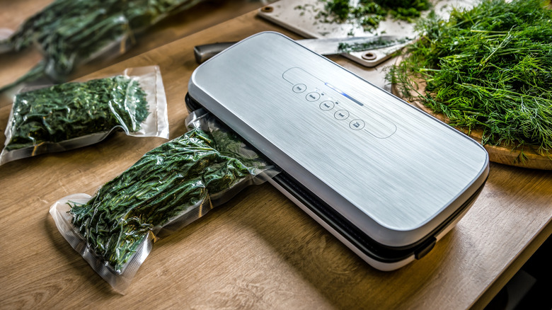 Vacuum sealing machine sitting on a wood countertop being used to vacuum seal herbs
