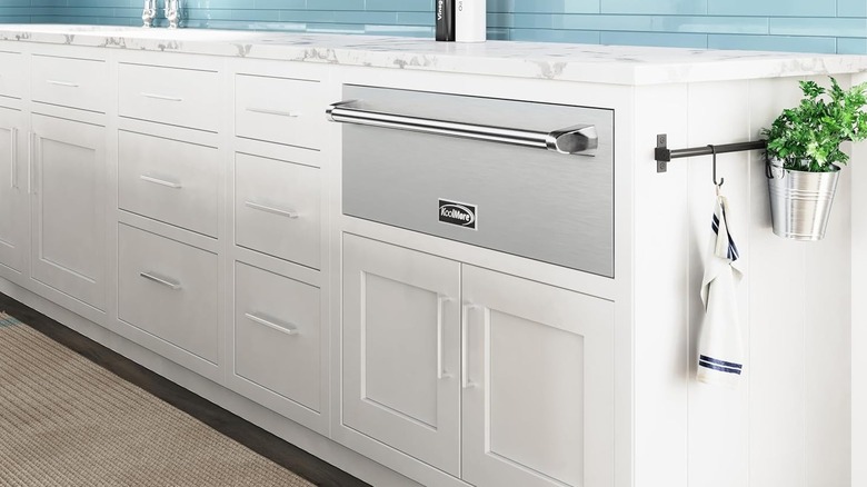Kitchen with a stainless steel warming drawer built into the white cabinets