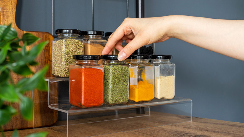 Person's hand puts away a spice jar on a spice rack