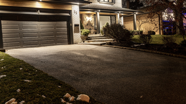 A dark driveway at night with the only light coming from the house.