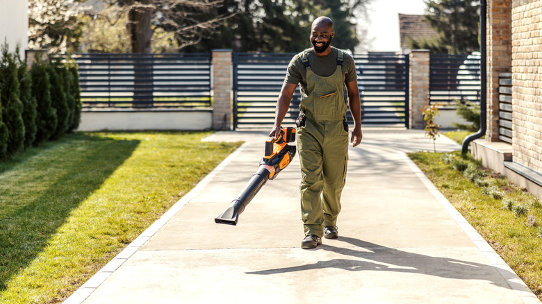 A man walking up the driveway to a home with a leafblower in hand
