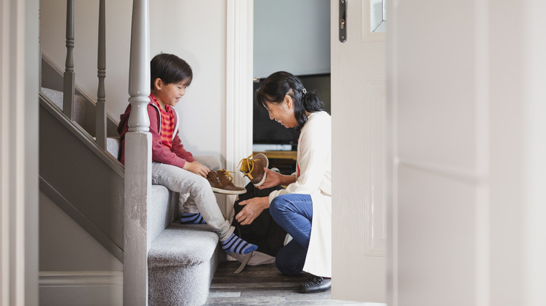 woman helping boy put shoes on while sitting on staircase in entryway
