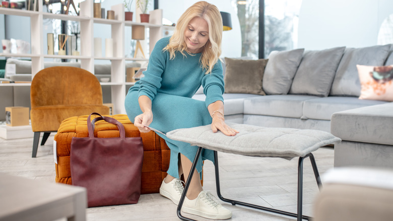 Woman sitting on velvet futon in a furniture store looking at price tag.