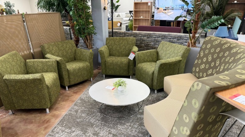 Four green chairs and a booth arranged around a white coffee table at a furniture liquidation store.